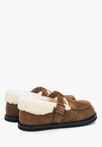Brązowe zamszowe kapcie z miękkim białym futerkiem w środku i regulowanym paskiem. Płaska czarna gumowa podeszwa z wykończeniem szwów w górnej części.