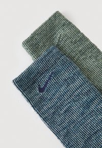 Nike nogavice z strukturiranim rebrastim vzorcem v temno zeleni in modri barvi, z kontrastnimi temno modrimi logotipnimi akcenti.