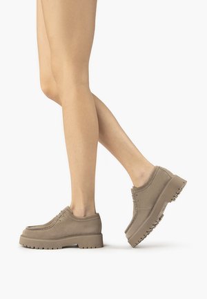 Beige semišové boty s tlustou gumovou podrážkou, kulatou špičkou a dekoračním prošitím. Design má minimální detaily šněrování a texturovaný svršek.