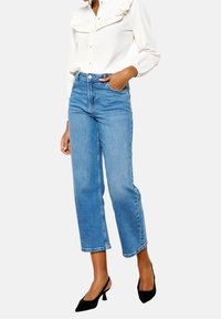 Ljusblå denim cropped jeans med hög midja och rak ben. Kombinerat med en vit blus med rufflade detaljer och svarta klackar.