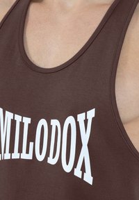 Brązowy bawełniany tank top z okrągłym dekoltem i białym nadrukiem, na którym widnieje napis "MILODOX". Gładka tekstura i sportowy krój.