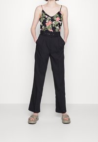 Pantaloni neri a vita alta con un design a gamba larga, dotati di una cintura e tasche laterali, abbinati a un top senza maniche con stampa floreale e sandali neutri.