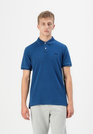 Polo bleu avec un col, des manches courtes et un logo GAP discret. Fabriqué en tissu texturé, associé à un pantalon de survêtement gris.