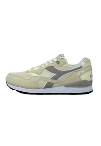 Sneaker beige chiaro con una tomaia texture, dettagli grigi e una suola bianca. Presenta lacci e un logo visibile sul tallone.