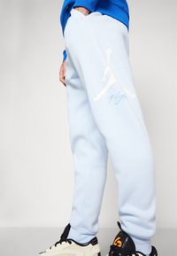 Calças de treino azul claro, feitas de material suave, apresentam um logo branco da Jordan e o texto "Flight" na coxa esquerda, com punhos elásticos.
