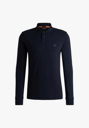 Polo à manches longues bleu marine en coton, avec un col classique, deux boutons et un écusson logo sur la poitrine. Texture douce.