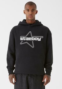 Černá mikina z bavlněné směsi, se přední kapsou v klokaním stylu a velkou bílou hvězdou a textem "starboy" potištěným na hrudi.