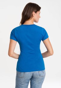 Blue fitted t-shirt made of cotton, featuring short sleeves and a round neckline, worn with light blue jeans. Smooth texture, no patterns.