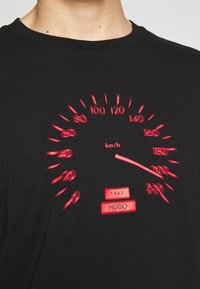 Czarny t-shirt z graficznym wzorem czerwonego prędkościomierza z oznaczeniami do 200 km/h. Zawiera napis "1993" oraz "HUGO" na dole.
