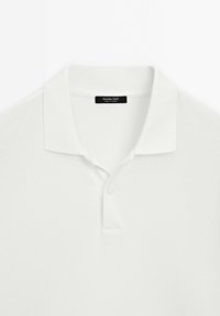 Bílá polo košile s límečkem, dvouknoflíkovou légou a texturovanou tkaninou. Štítek nese nápis "Massimo Dutti, vyrobeno v Turecku."