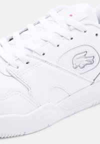 Baskets blanches avec une tige synthétique lisse, des lacets plats, un logo embossé et une semelle en caoutchouc texturée avec un bout arrondi.