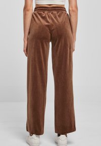 Brązowe, szerokie, aksamitne spodnie z elastycznym pasem i sznurkiem. Połączone z białymi sneakersami, ukazując gładką teksturę i czyste linie.