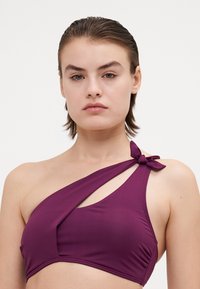 Top bikini viola a spalla unica con design intrecciato e dettaglio a fiocco. Tessuto morbido e testurizzato con silhouette minimalista.