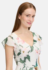 Kwiatowa sukienka z lekkiego materiału z dekoltem w serek. Posiada różowe i zielone wzory kwiatowe oraz fale rękawów, co zapewnia miękką teksturę.