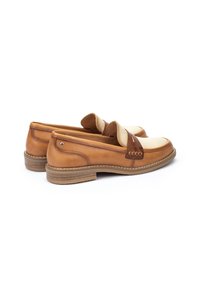 Zapatos de piel marrón tipo slip-on con un empeine color crema, que cuentan con una correa en el medio del pie y una suela de goma texturizada. Acabado liso.