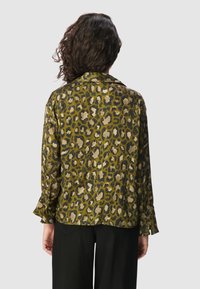 Koszula w wężowy wzór w oliwkowym kolorze, z kołnierzykiem, długimi rękawami z rozszerzanymi mankietami oraz lekką, gładką teksturą.