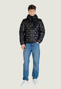 Czarna pikowana kurtka puchowa z kapturem, zapinana na zamek, z kieszenią na piersi; w zestawie z niebieskimi dżinsami i białymi trampkami.