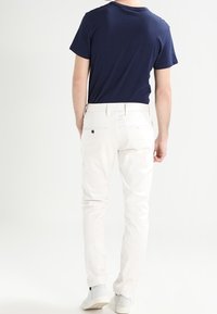 Marinblå t-shirt med kort ärm och vita slim-fit byxor, som visar upp rena linjer och en enkel design. Byxorna har en bakficka med en svart knapp.