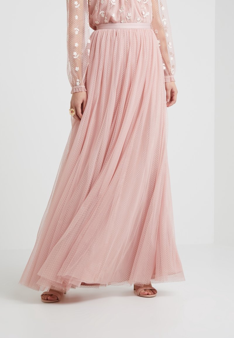Jupe fluide en tulle rose à petits pois, associée à un chemisier transparent brodé de fleurs et des talons ouverts.