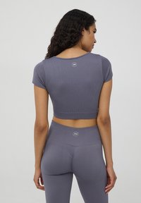 Szary, prążkowany top z krótkim rękawem, z logo z tyłu. W połączeniu z szarymi legginsami o wysokim stanie, o gładkiej fakturze i dopasowanym kroju.