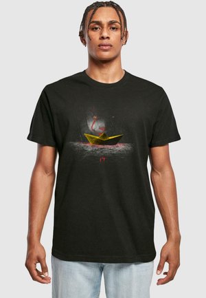 Black cotton t-shirt featuring a graphic of a yellow paper boat and a red-faced figure against a misty background. Standard fit.
