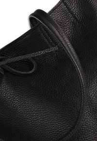 Sac en cuir noir avec une finition texturée, forme arrondie et une fermeture fine nouée. Il présente des bords lisses et un design épuré.