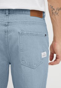 Šviesiai mėlyni džinsai su lygiu paviršiumi, su užpakaliniu kišenėle, oda žyme "DENIM JOURNEY" ir siuvinėjimo detalėmis.