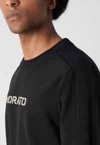 Sudadera negra con paneles de hombro acanalados y un logotipo texturizado. Tejido suave con cuello redondo y diseño ajustado.
