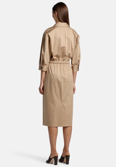 Beige cotton dress with a loose fit and half sleeves, featuring an elastic waistband and a knee-length cut. Includes buttoned cuffs.