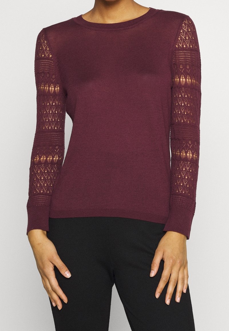 Burgunderfarbener Strickpullover mit langen Ärmeln; Spitzenakzente an den Ärmeln; gerippter Halsausschnitt und Bündchen; figurbetonte Silhouette; weiche Textur.