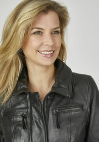 Schwarze Lederjacke mit hohem Kragen, Reißverschluss vorne und zwei Reißverschlusstaschen mit Quasten. Glatte Textur mit genähten Akzenten.