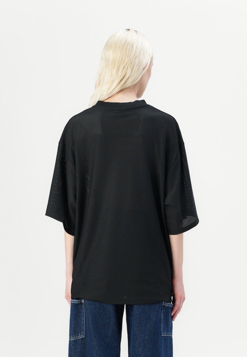 T-shirt noir en maille surdimensionné avec des manches courtes, doté d'un col rond et d'une coupe ample. Tissu texturé avec des perforations pour la respirabilité.