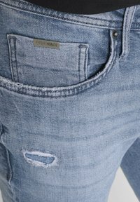 Svijetloplave traperice s istrošenim detaljem na bedru i metalnom oznakom "ANTONY MORATO" na stražnjem džepu.