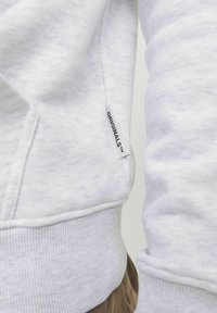 Sudadera gris hecha de una tela suave, con un dobladillo y puños acanalados, y una pequeña etiqueta de "ORIGINALS" en el costado cerca del dobladillo.