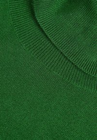 Gros plan sur un tissu tricoté vert montrant une texture côtes et un bord plié, mettant en valeur les points détaillés et le tissage du matériau.