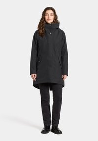 Svart vattentät parka med hög krage, två framfickor och en något längre bakdel. Slät textur, minimalistisk design.