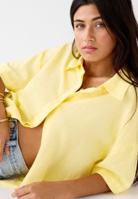 Geel linnen overhemd met knopen, korte mouwen, een relaxte pasvorm en een zachte textuur, gecombineerd met high-waisted denim shorts.