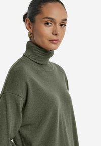 Grüner Strick-Turtleneck-Pullover mit lockerer Passform, mit geripptem Muster am Kragen und weiten Ärmeln. Minimalistisches Design.