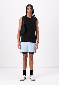 Débardeur noir sans manches, shorts en maille bleu clair avec des bordures noires, sac en bandoulière noir et baskets blanches/black avec des semelles texturées.