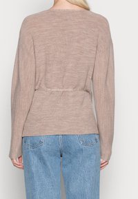 Beige ribbad tröja med långa ärmar, cinchad midja och rund halsringning, i kombination med ljusblåa, löst sittande jeans.