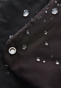 Wassertropfen perlen auf dunklem, wasserabweisendem Stoff mit einer sichtbaren Metallösen in einer Ecke.