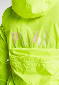 Fluorescent yellow jacket with hood, featuring a reflective Puma logo, zippered pocket, and smooth, lightweight fabric.