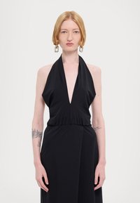Svart halterneck-kjole med dyp V-hals, innsnevring i livet og drapert stoff. Har en jevn tekstur og et minimalistisk design. Justerbare snorer ved halsen.
