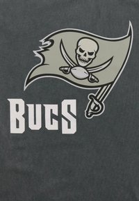 Šedá látka s velkým zeleným grafickým motivem pirátské vlajky. Na vlajce je lebka s překříženými meči, doplněná textem "BUCS" tučnými bílými písmeny.