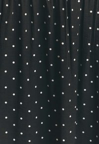 Černá tkanina s bílými puntíky, s jemnou texturou a sklady. Puntíky se liší velikostí a jsou rovnoměrně rozmístěny.