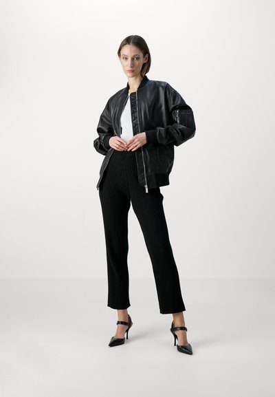 Black leather bomber jacket with a ribbed collar, zip closure, and side pockets, paired with black ribbed trousers and pointed heels.
