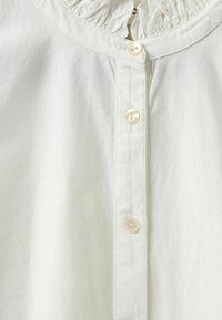Biela bavlnená košeľa so zúženým výstrihom, s predným zapínaním na gombíky a jemnou textúrou. Štandardný strih, ľahká látka.