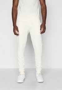 Cremefarvede sweatpants i slim fit design med elastiske cuffs, med en diskret logo detalje, parret med hvide sneakers.