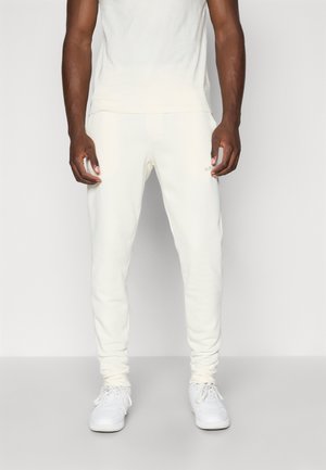 Kremfargede sweatpants i slim fit-design med elastiske mansjetter, som har en subtil logodetalj, kombinert med hvite sneakers.