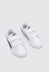 Sneakers bianchi con una superficie liscia, strap con velcro e un accento nero lungo il lato, con un logo sulla linguetta.